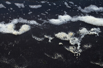 Ocean waves creating white foam on a black-sand beach.