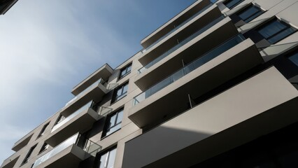 Modern residential building facade showcasing contemporary architectural design with multiple glass balconies against a bright blue sky.