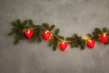 Top view of green pine garland decorated with glowing light and soft red felt heart for romantic winter Christmas holiday background
