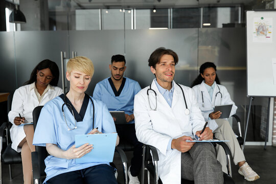 Education and Training for Health Care Professionals Concept. Multiethnic group of doctors in workwear attending medical conference or training at clinic, holding medical charts, using digital tablets