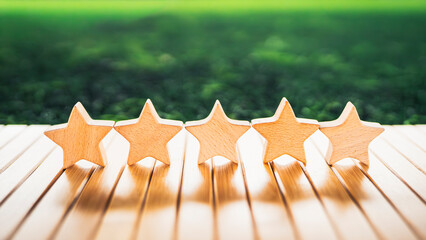 Five wooden stars neatly aligned on wooden surface with green blurred background, symbolizing customer satisfaction, five-star rating, product quality, and positive reviews.