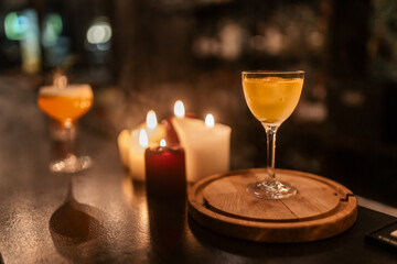 A finished cocktail presented in a dark, moody atmosphere with candlelight and a touch of mist.