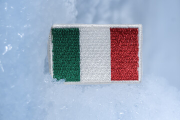 Italian flag patch embedded in glacial ice, symbolizing winter travel, alpine identity, and Italy’s northern snow regions. A minimalist scene linking national culture with cold-climate exploration.