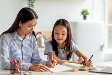 Mother and daughter sit at the kitchen table, engaged in drawing with colorful markers. They share a joyful moment, creating art together in a bright and inviting space.