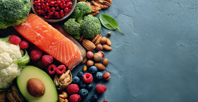 Fresh salmon fillet surrounded by vibrant vegetables, nuts, and berries on a textured blue surface, showcasing healthy eating and nutrition concepts with copy space