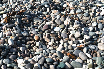A serene coastal scene showcases smooth, colorful pebbles under bright sunlight. This luxurious setting invites relaxation, ideal for spa treatments by the sea.