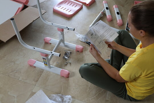 Woman assembling children's furniture made of metal and plastic while reading instructions with screws and bolts around