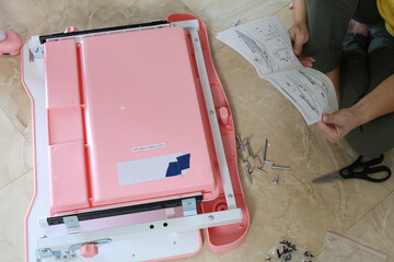 Girl examining assembly instructions for kids furniture, metal components and fasteners scattered around her on the floor