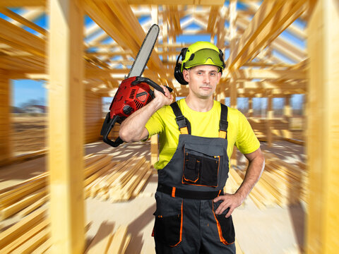 Wood construction worker prepares timber cutting with a chainsaw, performing structural carpentry tasks during wooden frame building assembly on site.