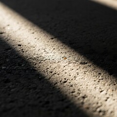 A dramatic shaft of sunlight cutting across a dark, textured concrete surface, creating high-contrast light and shadow