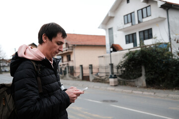 A man stands by the road checking his phone. The moment reflects daily navigation and the concept of routine communication.