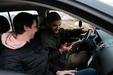 Two men sit inside a car while one checks information on a smartphone. The scene reflects navigation, planning, and road assistance.