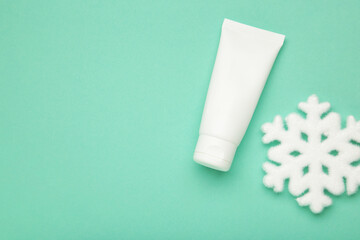 Winter skin care concept. Cosmetic moisturizer cream and snowflakes on mint background.
