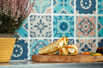 A fresh chicken wrap on a wooden board, styled in a bright cafe with decorative Mediterranean tiles...