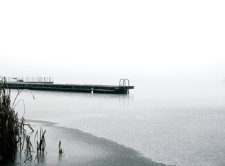 Winter pier in fog A frozen lake with a lone pier and reeds fading into milky fog. Minimalist, cold...