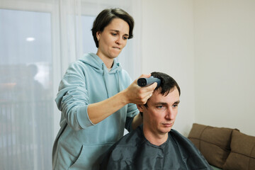 A woman uses a trimmer to shorten a man s hair during a home haircut. The moment reflects personal grooming and the concept of everyday care.