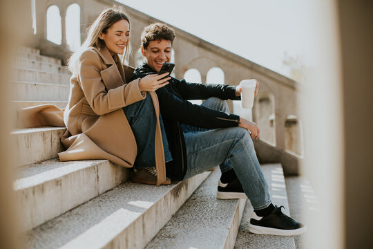 Couple enjoying a relaxed moment on stairs while browsing on a smartphone - Powered by Adobe