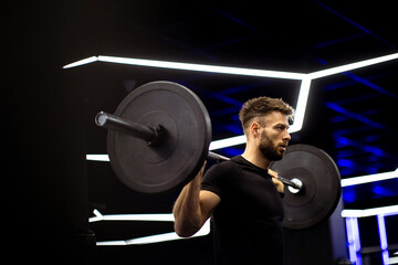 Strong man lifting weights in a modern gym surrounded by dynamic lighting