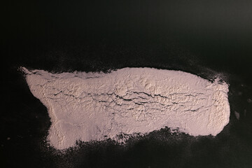 Close-up still-life of a scattered layer of flour on a dark green surface, showcasing its fine texture, soft shadows, and organic, natural pattern.