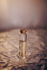 Atmospheric close-up of a small glass vial filled with clear liquid, sealed with a cork stopper, standing on a dark textured surface with warm, moody lighting highlighting droplets inside the bottle.