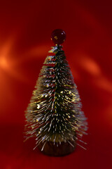 A small decorative Christmas tree with a wooden base, covered in white glitter, standing on a bright red background.