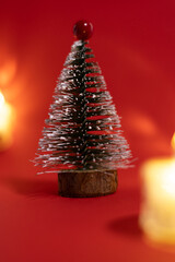 A small decorative Christmas tree with a wooden base, covered in white glitter, standing on a bright red background.