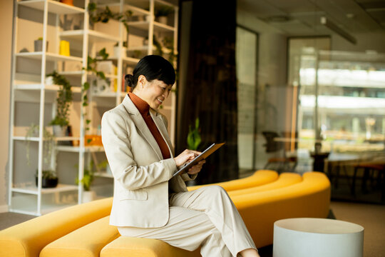 Professional woman using tablet in modern office lounge during daytime work hours
