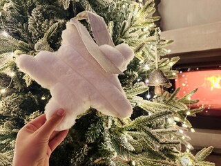 Hand Decorating Christmas Tree with Star Topper and Fireplace Burning Behind – Warm Festive Setting