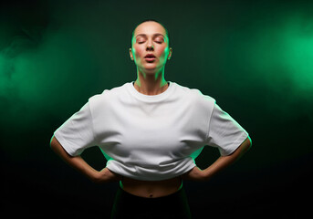 Sporty young woman taking deep breath with eyes closed, feeling calm and focused in dramatic green neon studio lighting with smoke effect