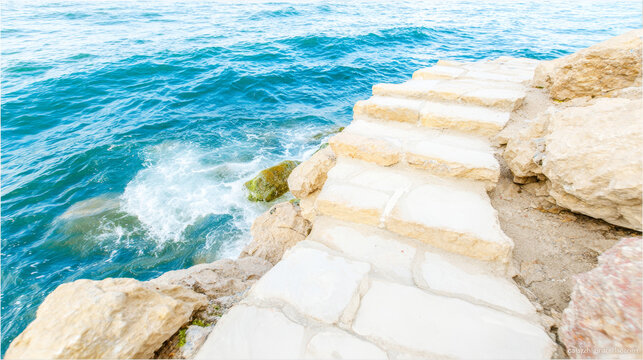 Old stone staircase descending into vibrant blue sea water, creating an inviting path to the ocean and coastal rocks - Powered by Adobe