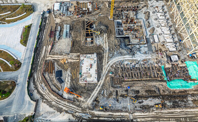 Aerial view of a busy construction site with heavy machinery and foundations on ground.