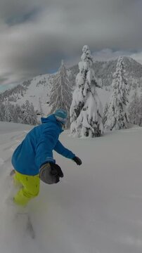 POV: Snowboarder enjoys riding fresh powder snow on a closed alpine ski resort. Freerider is carving among snowy spruce trees with stunning views of white mountains. Winter fairy tale in highlands.