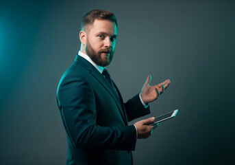 Confident bearded businessman holding digital tablet and gesturing with hand, looking at camera with dramatic teal rim lighting for corporate concept.