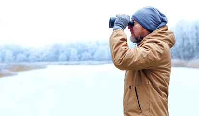 Ecologist man with binoculars observing the frozen winter forest. Environmental research and wildlife conservation in nature. Winter nature research and environmental protection work.