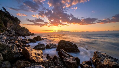 Vivid sunset over a rocky beach, ocean waves shimmering, and the cloudy sky illuminated with golden light