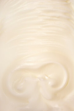 An abstract close-up of glossy, stiffly beaten egg whites forming soft peaks and swirling, creamy texture.