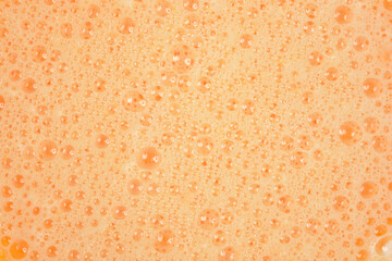 An abstract, full-frame close-up of a vibrant orange, foamy mixture composed of many small bubbles