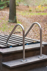 Metal handrail on a wooden platform in an autumn park, railing for descent, close-up of the structure