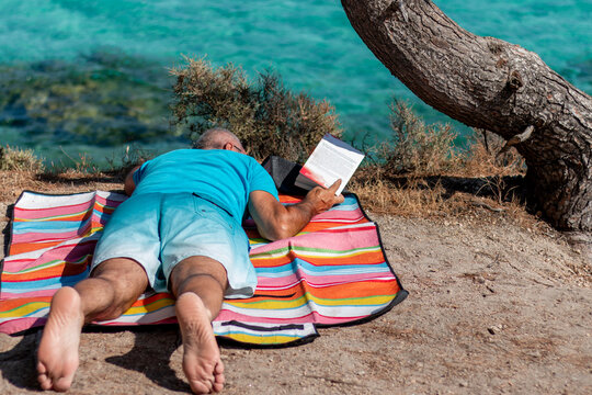 Senior man relaxing reading book by clear turquoise sea