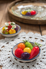 A beautifully arranged selection of colorful Thai Luk Chup—miniature fruit-shaped mung bean desserts—presented in small ceramic bowls with traditional blue-and-white patterns. 