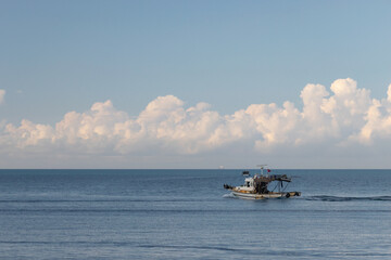 Small Fishing Boat Navigating Calm Open Sea Under a Wide Blue Sky Dominated by Huge, Fluffy White Clouds, Conveying a Sense of Serene Independence.