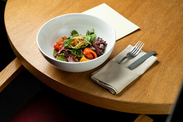A vibrant garden salad blends colorful vegetables with fresh greens in a inviting bowl on a smooth wooden table. Natural light enhances the atmosphere of the cozy setting