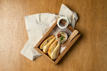Freshly baked bread slices are neatly arranged on a simple wooden tray accompanied by a small jar of flavorful spread. The warm ambiance enhances the inviting meal experience