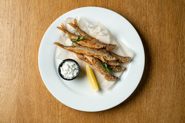 A plate displays freshly fried fish, crispy and golden. A wedge of lemon adds brightness, while a small bowl of dipping sauce invites a delightful tasting experience