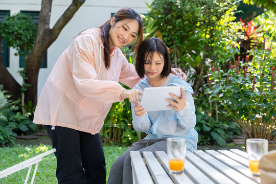 Digital Connection in Garden: Mother and daughter share a moment of digital connection in the garden, with a tablet displaying shared content in the tranquil space.