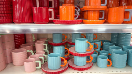 Colorful ceramic mugs and plates displayed on store shelves. Bright modern tableware in vibrant pastel tones, arranged neatly and ready for home decor or kitchenware shopping concepts.