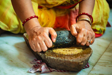Indian Woman Grinding Spices on Traditional sil batta or Stone Grinder in Kitchen.