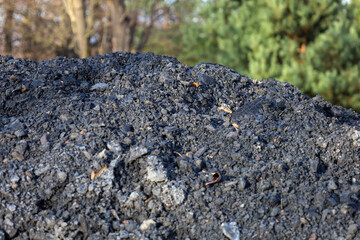 The foreground is dominated by a large pile of dark grey or black loose material, resembling fine gravel, coal, or construction soil, creating a rich texture.
