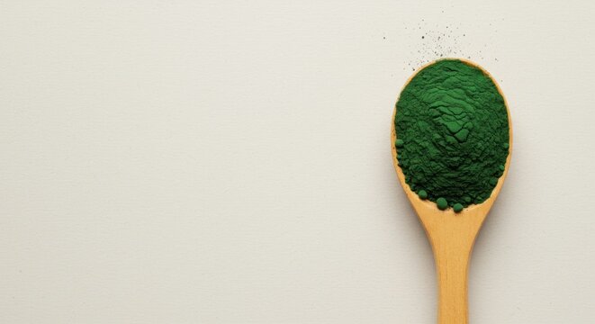 Green algae powder on wooden spoon against a neutral backdrop healthy food concept