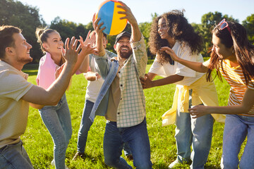 Happy joyful young people friends in casual clothes having fun in the summer park. Smiling men and women catching ball playing together outdoors on holidays. People and leisure in nature concept.